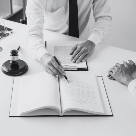 Vista superior de un bogado especializado en startups en su mesa de escritorio con un libro abierto al que señala con el bolígrafo en la mano y un cuaderno de notas